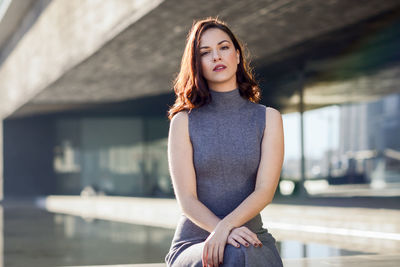 Portrait of young woman sitting outside modern building