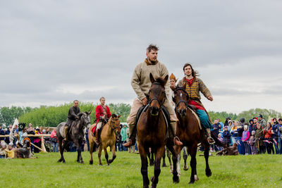 People riding horses on field against sky
