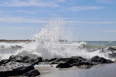 Waves splashing on rocks against sky