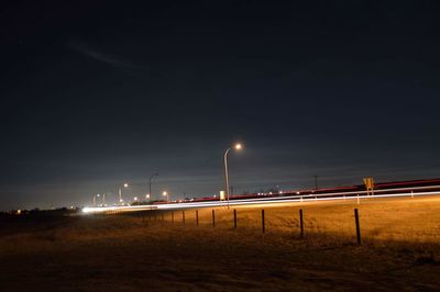 Light trails by field against sky at night