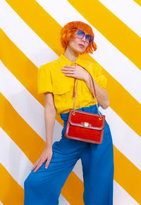 Retro model holding bag and wearing vintage look on trendy striped yellow background. minimal 