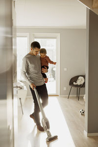 Father carrying toddler daughter while vacuum cleaning