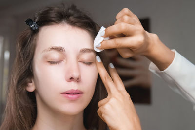 In a beauty salon, a master cosmetologist applies makeup and wipes eyebrows with a cotton pad. close