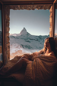 Woman relaxing on window against mountain