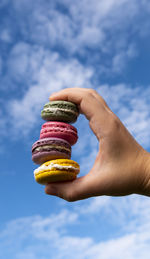 Midsection of person holding macaroons against sky