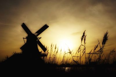 Silhouette windmill on field against sky during sunset