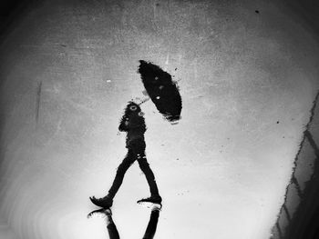 Reflection of person with umbrella on puddle at street