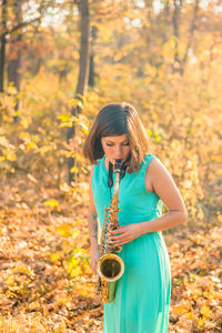 Young girl with black hair and a tattoo on her arm, dressed in blue dress and plays the saxophone