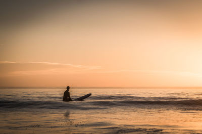 Man surfing in sea against sky during sunset