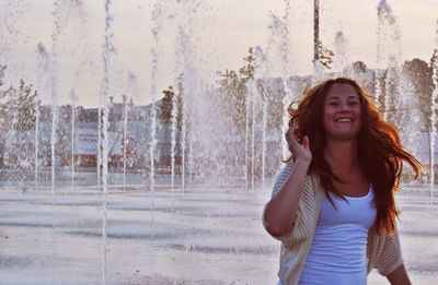 Happy woman standing amidst fountain