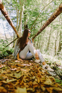 Full length of woman sitting by tree in forest