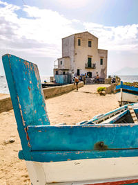 Fishing boats on beach by buildings against sky