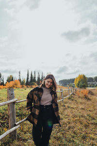 Portrait of young woman standing on field against sky