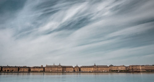 Buildings at waterfront against cloudy sky