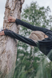 Rear view of woman hanging on tree at forest