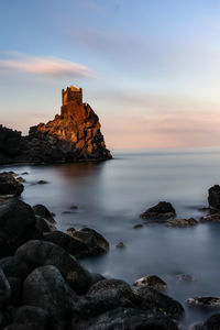 Rocks on sea shore against sky during sunset