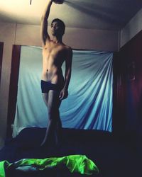 Full length of shirtless man standing on bed