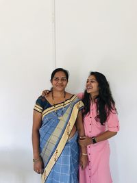 Smiling mother and daughter standing against white wall