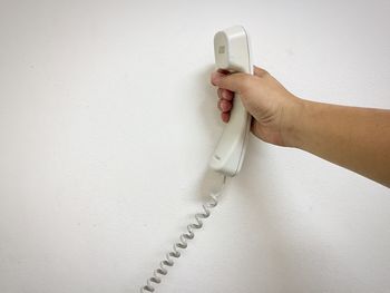 Close-up of human hand holding telephone receiver against wall