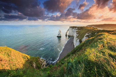 View of calm sea and rolling green cliffs against cloudy sky