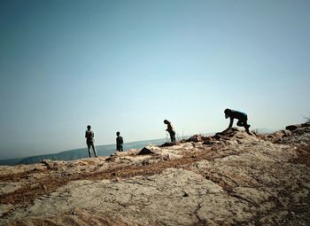 People standing on rock against clear sky