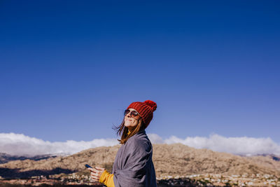 Side view of woman with umbrella against blue sky