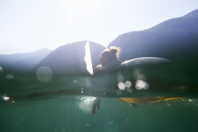 Woman lying on pool raft in lake against mountains during summer