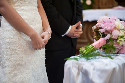 Midsection of couple standing by bouquet during wedding ceremony