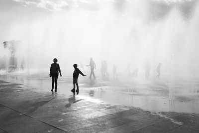Silhouette of people walking on wet beach during winter
