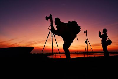 Silhouette people photographing on shore against sky during sunset