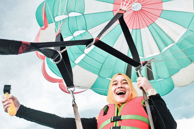 Low angle view of happy young woman paragliding against sky