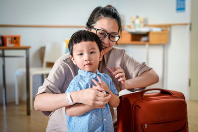 Mother with son standing by suitcase at home