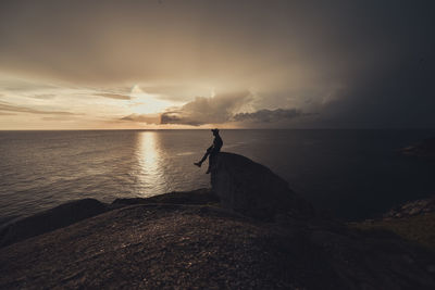 Silhouette man sitting on rock formation against sky during sunset