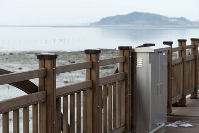 Wooden railing by sea against sky