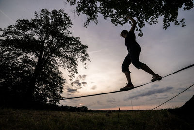 Silhouette man jumping on tree against sky