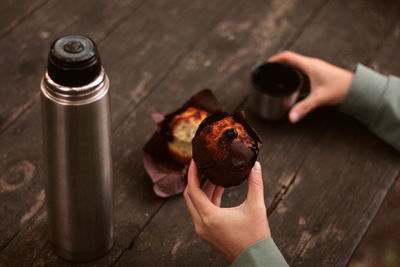 Muffin in female hands near a thermos on a wooden background outdoors