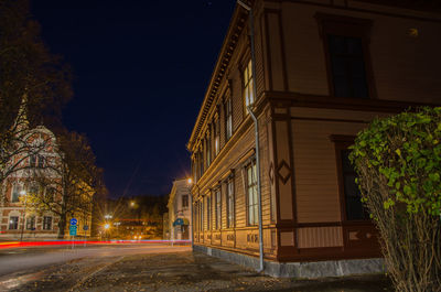 Empty road by illuminated buildings against sky at night