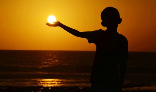 Optical illusion of silhouette boy holding sun at beach