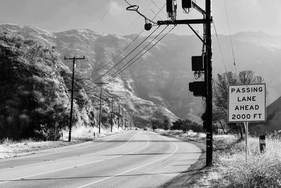 Road sign by trees and mountains against sky