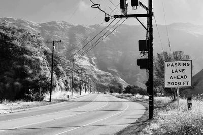 Road sign by trees and mountains against sky