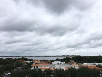 Houses by lake against cloudy sky