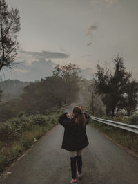 Rear view of woman walking on field against sky during sunset