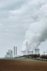 Smoke emitting from factory against sky