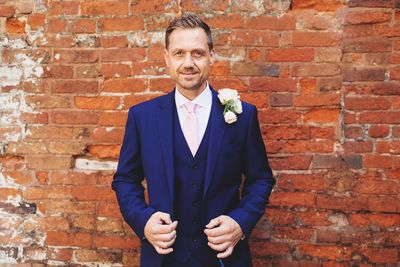 Portrait of handsome bridegroom wearing suit while standing against brick wall