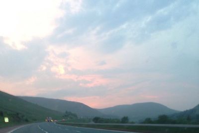 Country road by mountains against sky