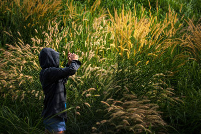 Side view of mid adult woman wearing hooded shirt standing amidst crops in farm