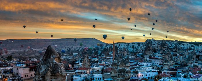 Hot air balloons over city against cloudy sky during sunset