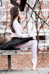 Side view of woman sitting against tree