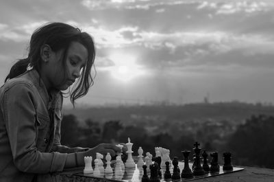 Portrait of young girl playing chess against cityscape 