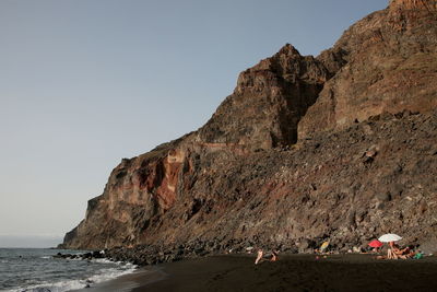 Rock formations on beach by sea against clear sky